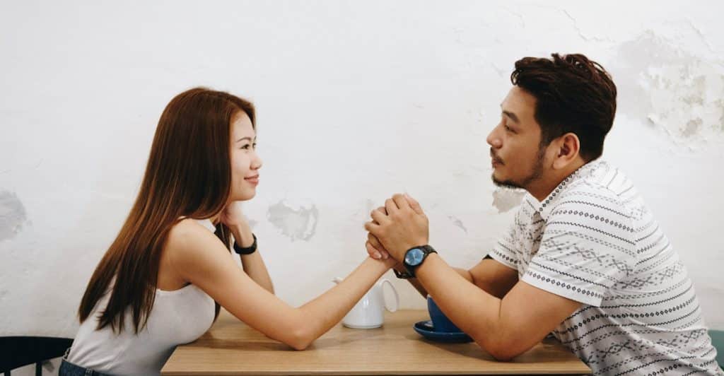 A couple sitting across from each other at a table, holding hands and gazing into each other's eyes.