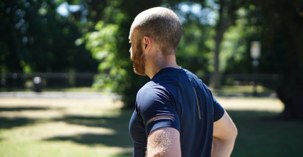 A man standing in a park, wearing athletic wear and looking away.