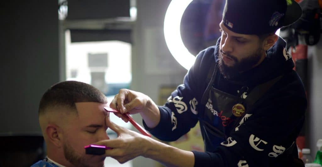 A barber is using clippers and a comb to shape the hairline of a client.