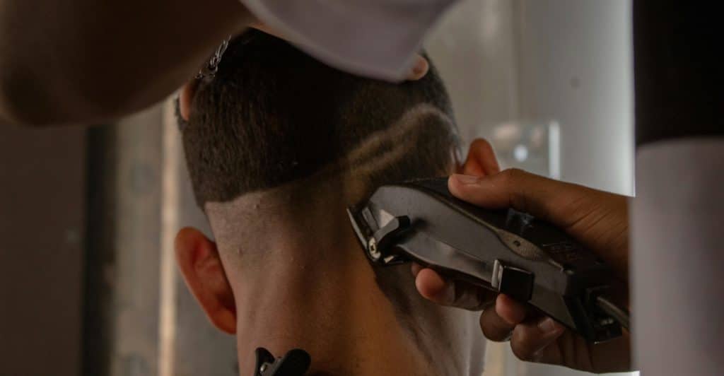 A barber giving a close-up haircut to a person with dark hair using an electric clipper.
