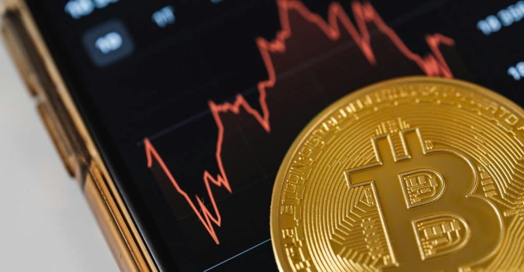 A close-up of a phone screen showing a stock market chart and a Bitcoin coin.