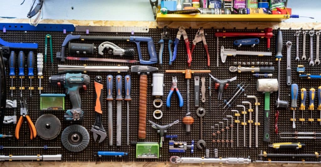 A black pegboard wall in a workshop, covered with a wide assortment of neatly organized tools.