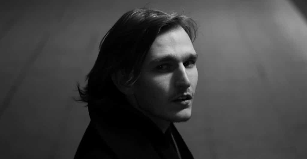 A black and white portrait of a man with medium-length hair.