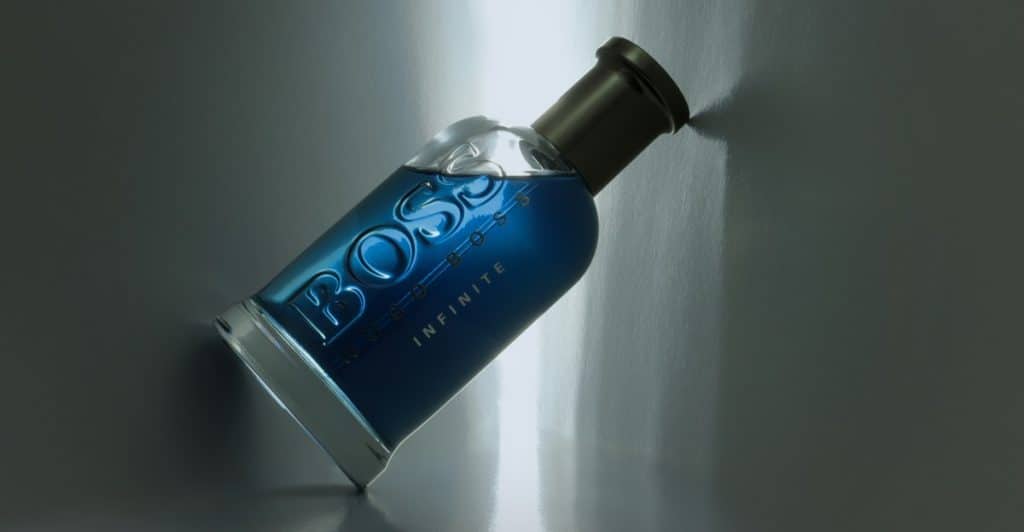 A bottle of blue "BOSS Infinite" fragrance tilted on a reflective surface.