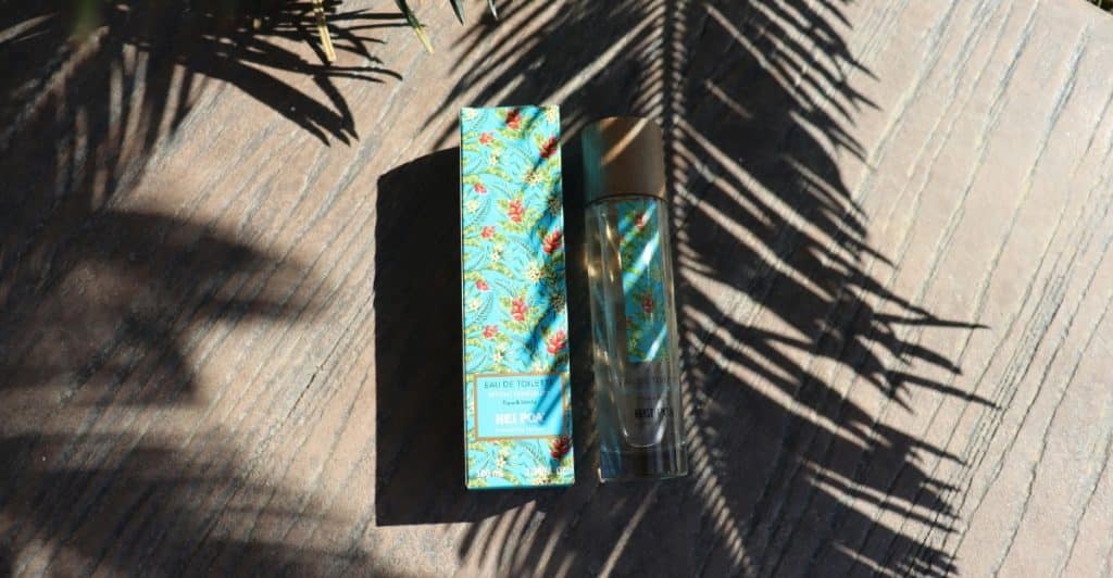 A bottle of fragrance with a box with a tropical pattern, placed outdoors with palm leaf shadows.