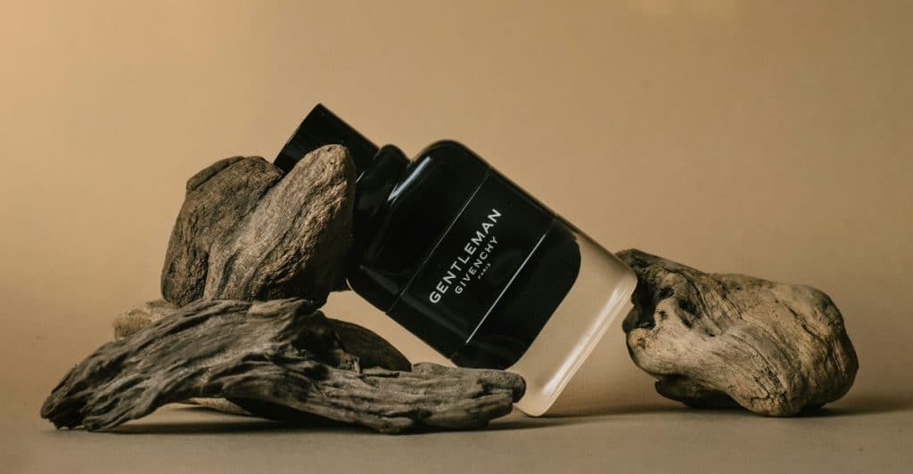 A bottle of black "GENTLEMAN GIVENCHY" fragrance resting on driftwood.