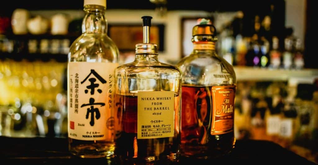 Three bottles of whiskey on a bar counter with a blurred background of a bar setting.