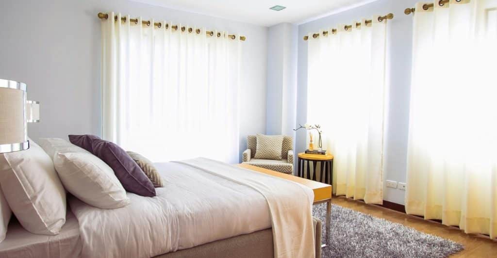 well-lit bedroom with a bed, pillows, a chair, and curtains, conveying a clean and calming space.