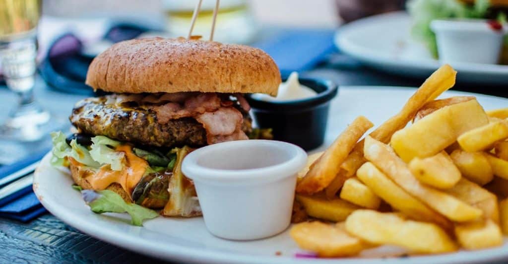 A burger with toppings and a side of french fries on a white plate.
