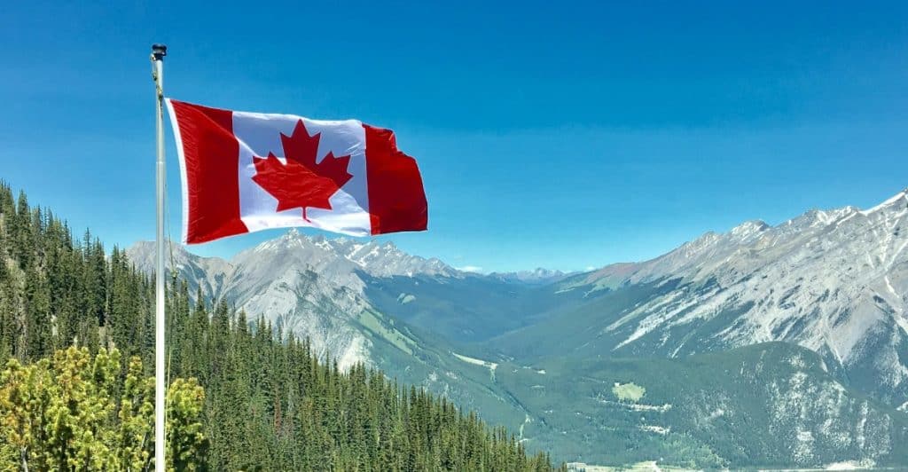 Canadian flag waving on a pole with a backdrop of snow-covered mountains.