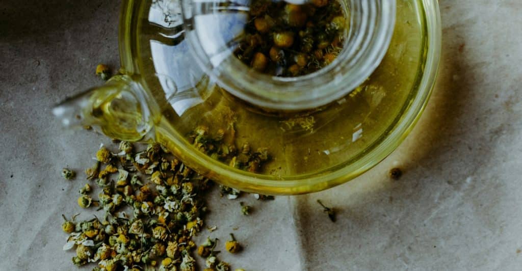 Dried chamomile flowers and a glass teapot on brown paper.
