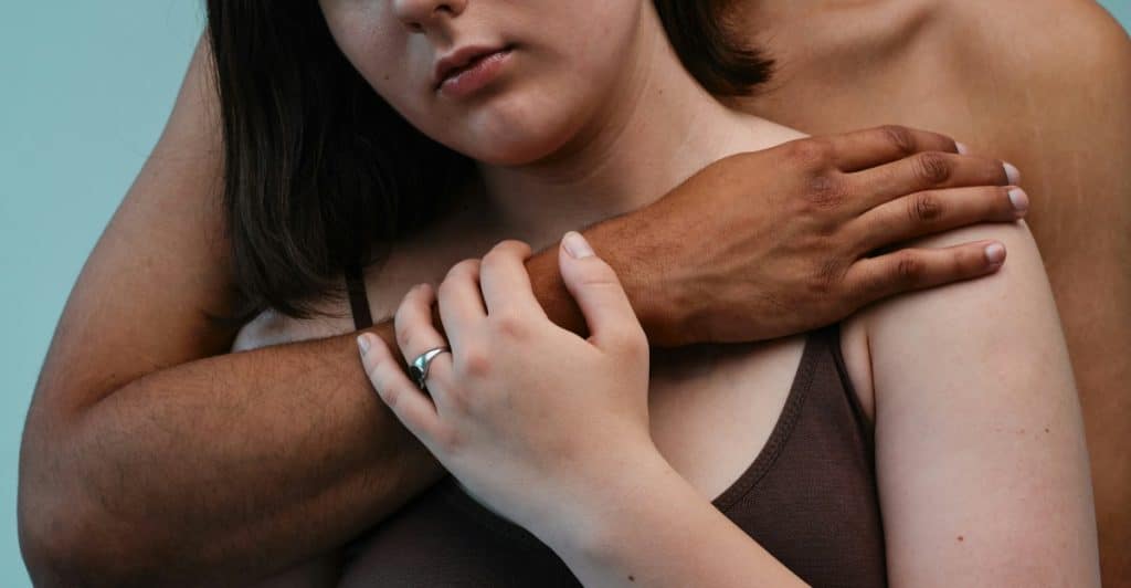 A close-up of two people embracing, showing hands clasped and arms around shoulders, suggesting support and closeness.