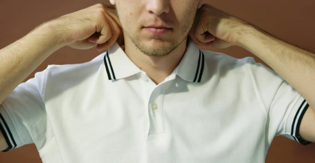 A close-up of a man's face and hands as he adjusts the collar of a white polo shirt with black stripes.