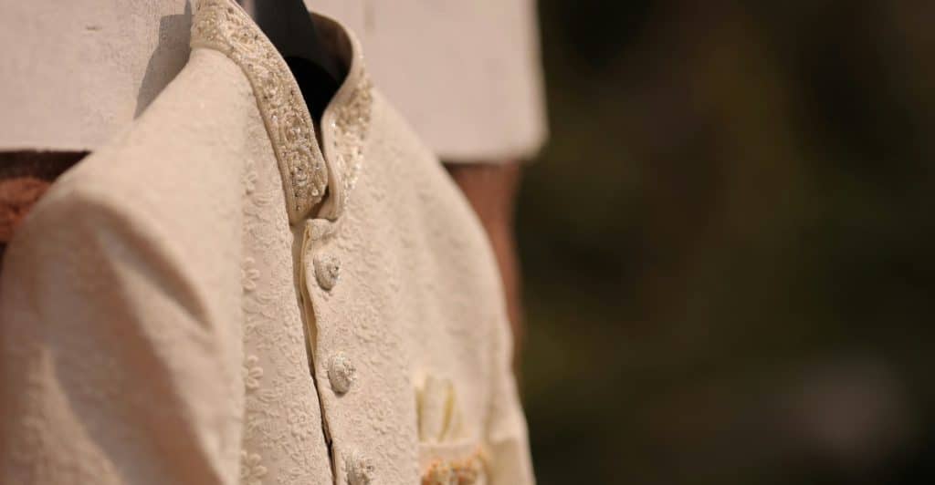A close-up of the embroidered collar and buttons of a cream-colored jacket.