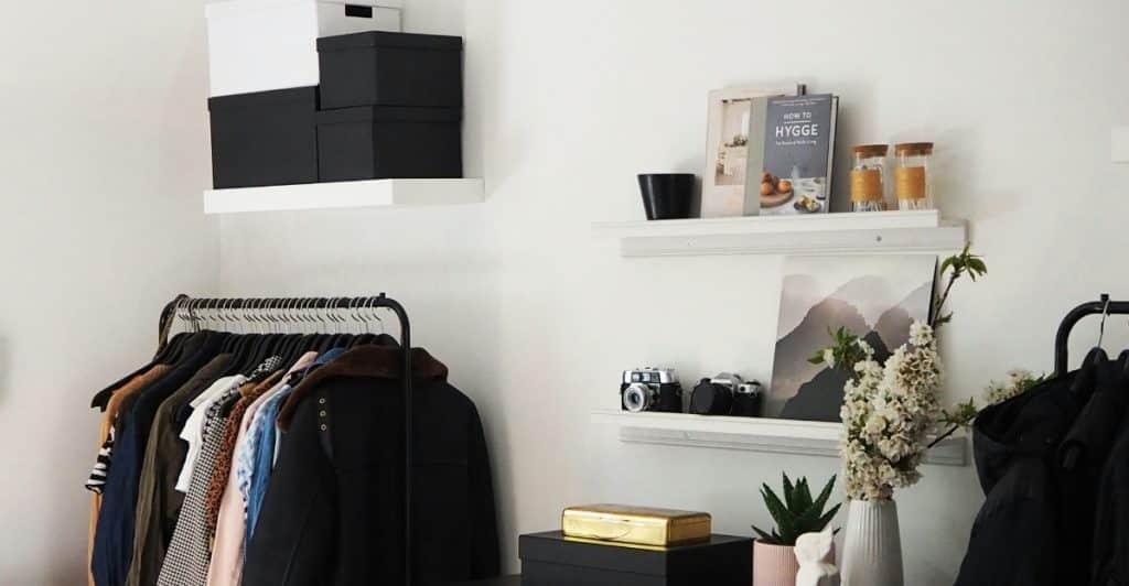 A clothing rack and shelves with clothes and decorative items in a room.