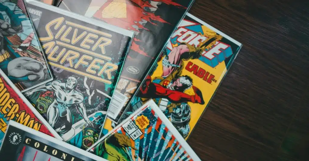A stack of comic books with colorful covers, including titles like "Silver Surfer," "Force Cable," and "Aliens Marine," lying on a wooden surface.
