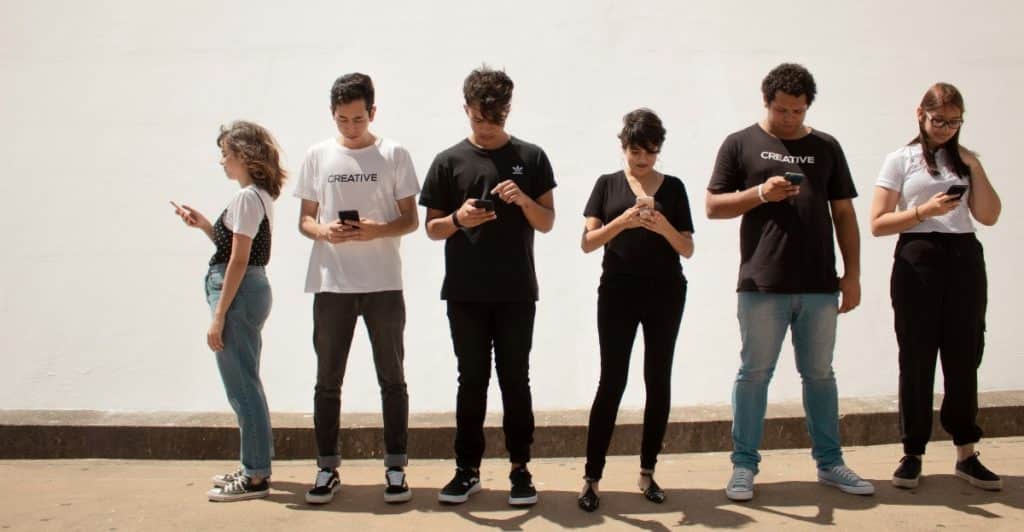 A group of people standing in a line, each using their smartphone.