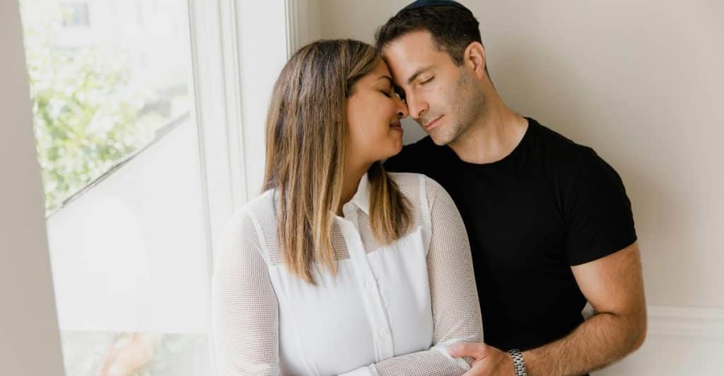 A man and a woman are standing close together, embracing in a room with natural light.