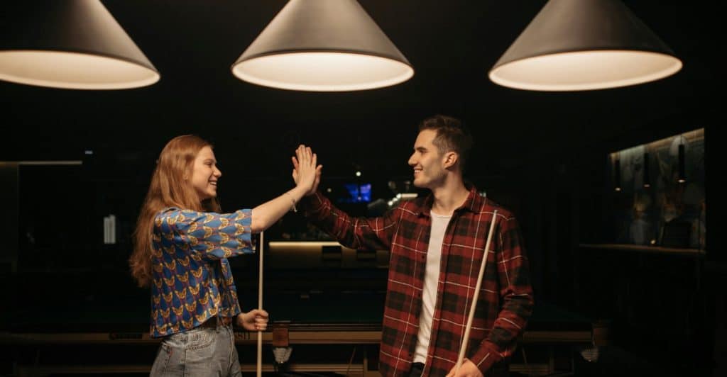A couple in a dimly lit room with pool tables, giving each other a high five and smiling, symbolizing appreciation and fun.