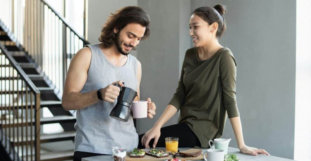 Couple having breakfast together, with the man pouring coffee while the woman smiles and looks at him.