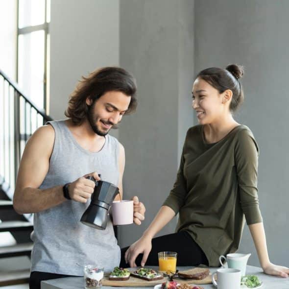 Couple having breakfast together, with the man pouring coffee while the woman smiles and looks at him.