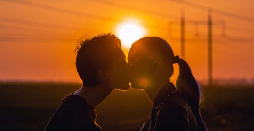 The silhouettes of two people kissing against the backdrop of a bright orange sunset, symbolizing romance.