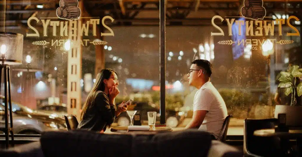  A man and a woman are seated at a table in a dimly lit restaurant, engaged in conversation.