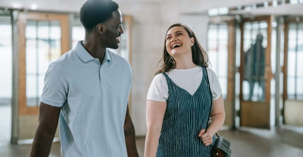 A man and a woman are walking together, holding hands and smiling, in an open space with doorways.