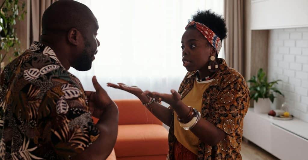 A man and a woman are arguing in a living room, gesturing with their hands
