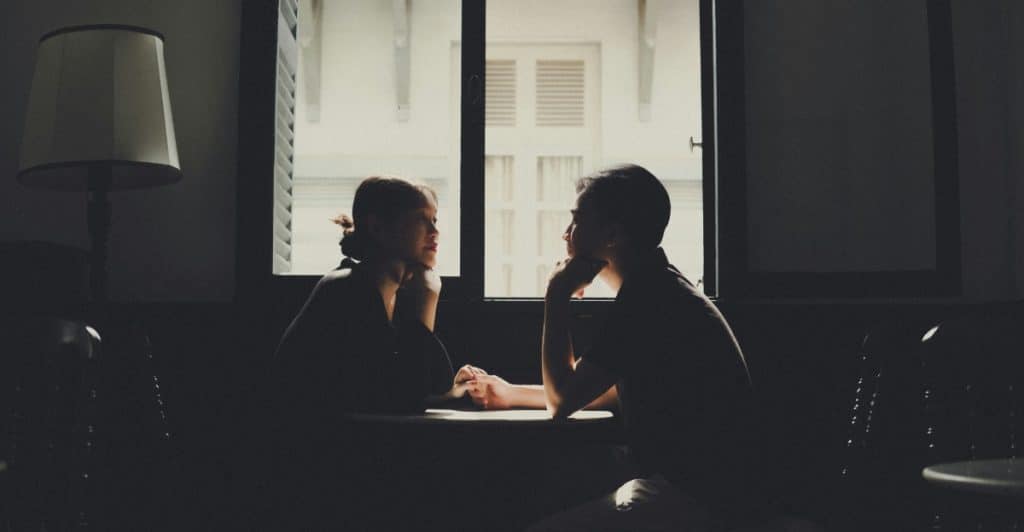 A silhouetted couple talking intimately at a table by a window.