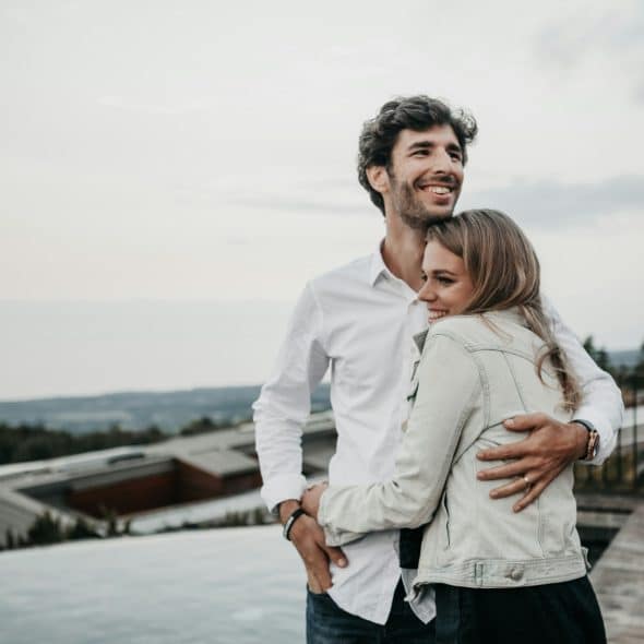 A couple embracing outdoors with a scenic background.
