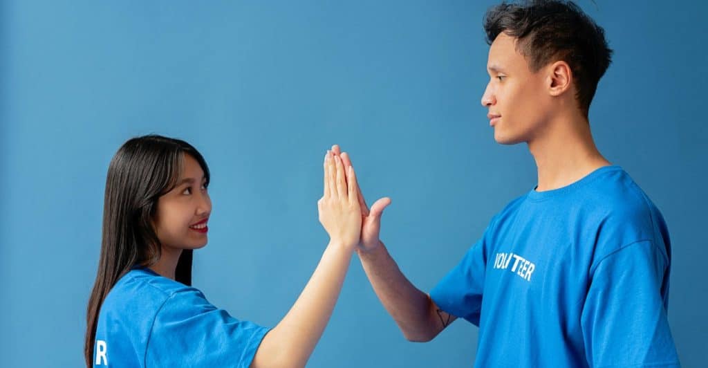 An Asian couple wearing matching blue shirts giving each other a high five against a blue background.