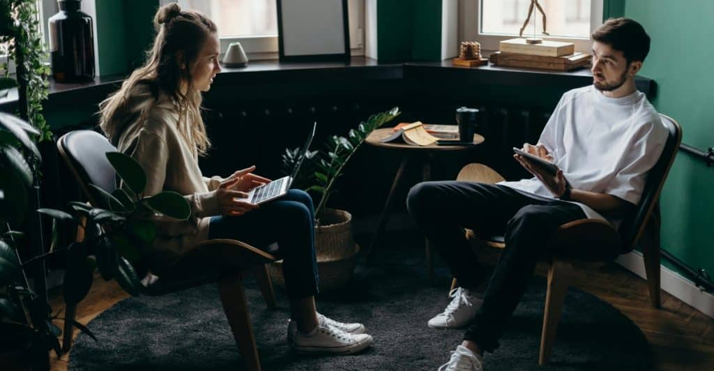 A man and a woman are sitting in chairs in a living room, having a conversation.