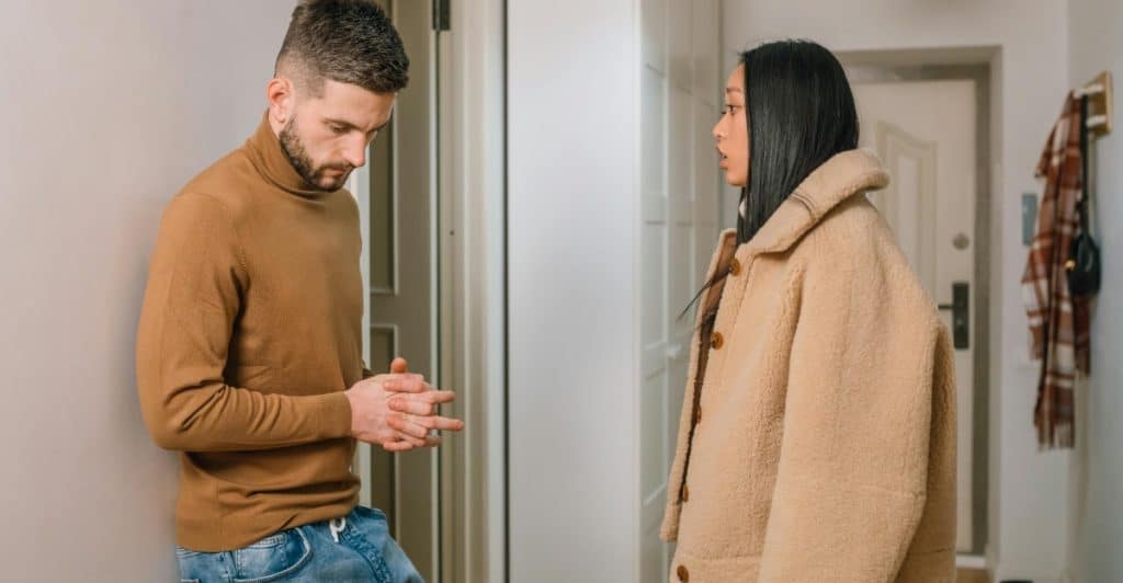A man and a woman are standing in a hallway, having a serious conversation.