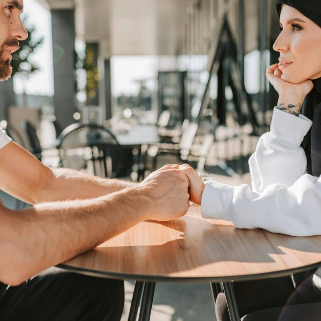 A man and a woman are sitting at a table, holding hands and looking at each other.