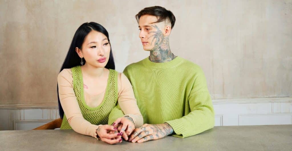 A couple sitting at a table, looking serious and holding hands.