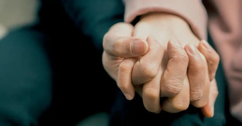 A close-up of two people gently holding hands, suggesting intimacy and support.