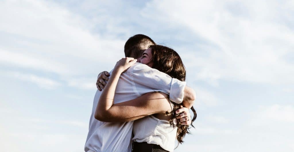 A couple hugging outdoors with a bright sky in the background.