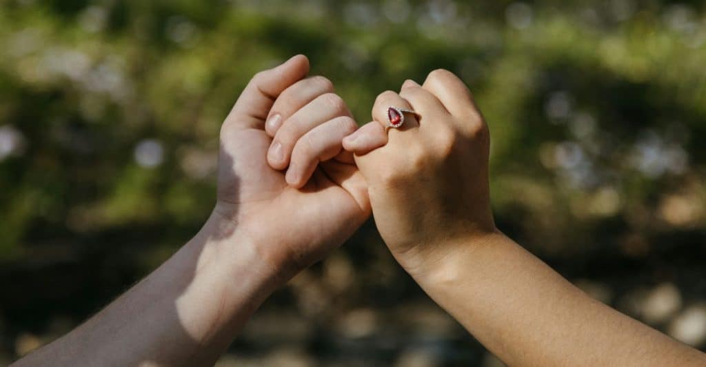 A close-up of a couple making a pinky promise with intertwined fingers.