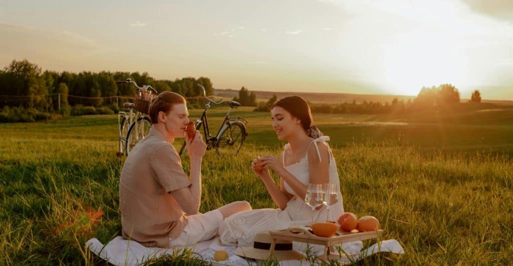 Young couple on a picnic at sunset with two bicycles parked in the background.