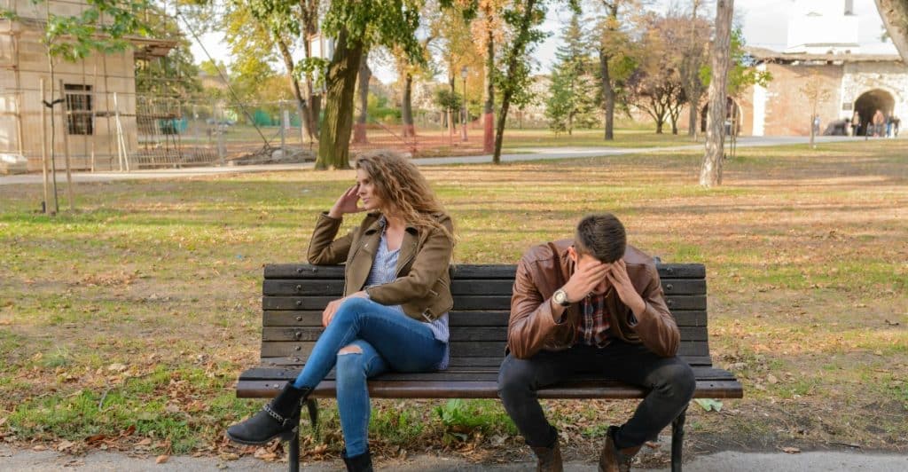 A couple sitting on a park bench, appearing distant or in conflict.