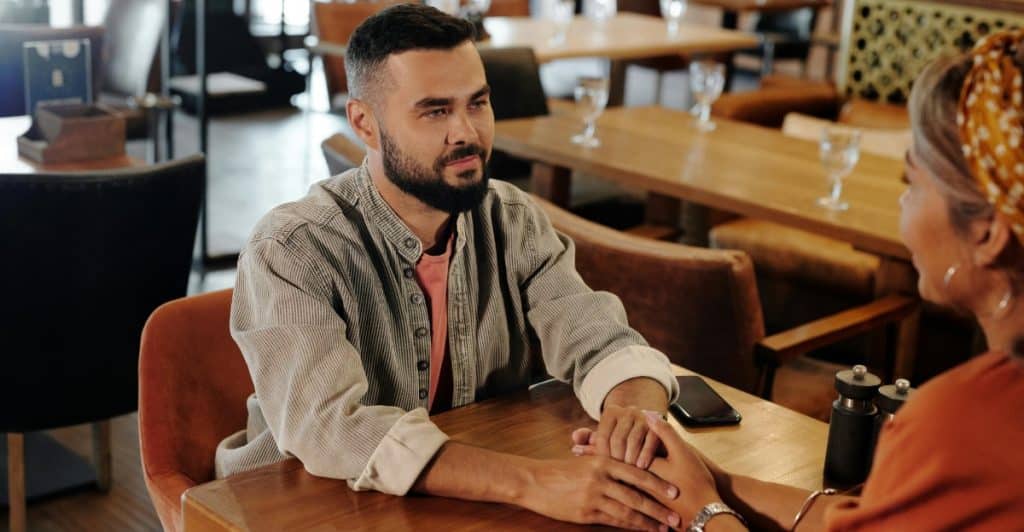 A man and a woman are sitting at a table, holding hands and looking at each other.