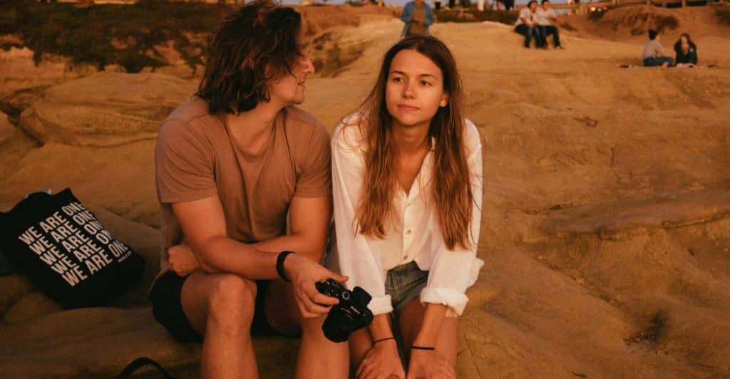 A man and a woman are sitting on a rocky outcrop, looking at each other.