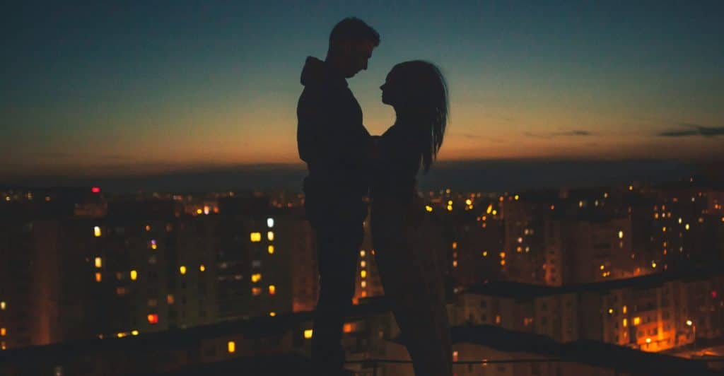 Silhouetted couple standing closely against a cityscape at dusk.