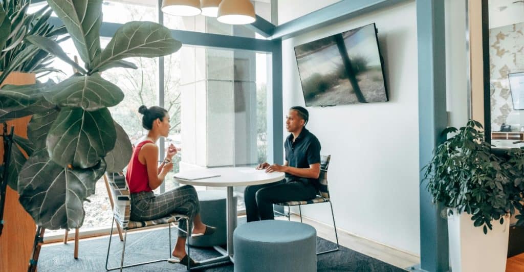  A man and a woman are sitting at a table in an office, having a conversation.