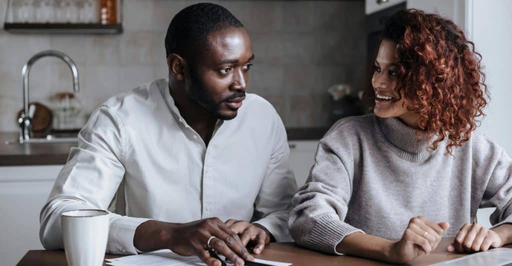 A Black couple sits at a table with papers and a laptop, engaged in a serious conversation.