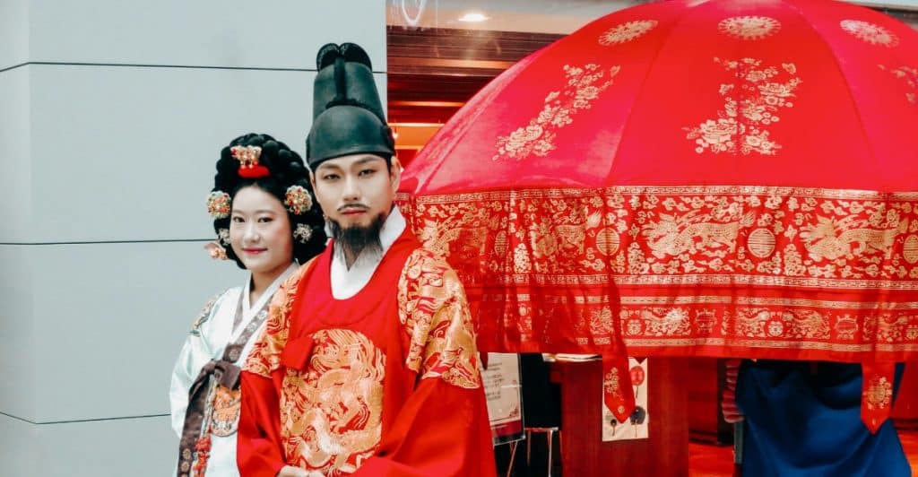 Couple wearing traditional Korean clothes with a large red umbrella behind them