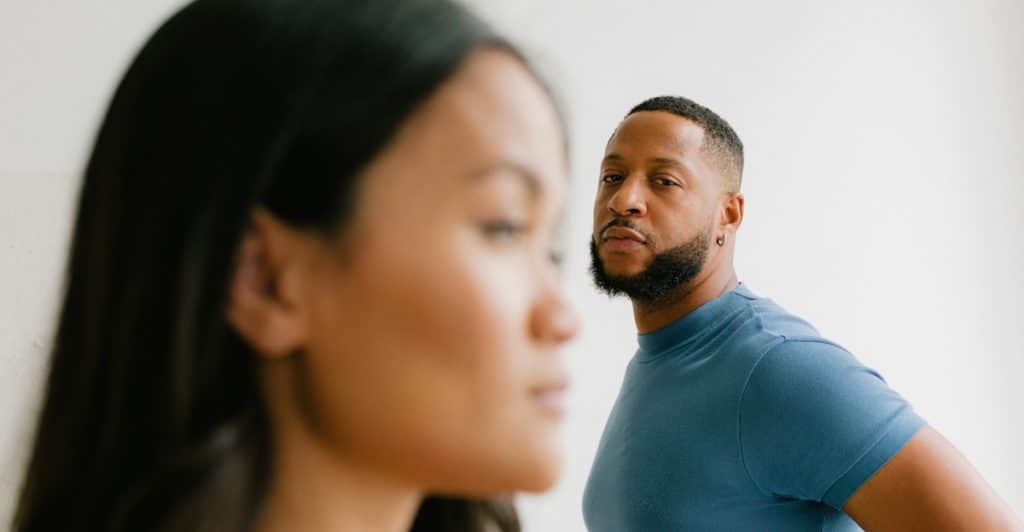 A person with long dark hair in soft focus in the foreground, while another person with a blue shirt looking towards them in sharper focus.