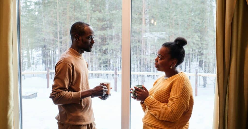 A couple standing by a window, having a conversation and holding mugs.