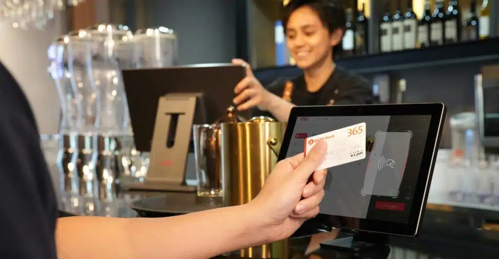  A person using a credit card to make a purchase at a point-of-sale terminal in what appears to be a bar or restaurant setting.